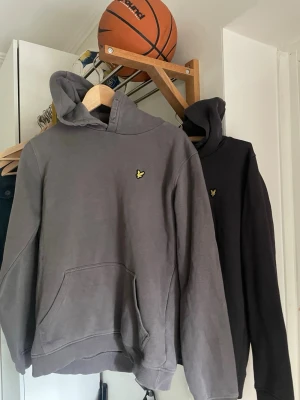 Grå hoodie från Lyle & Scott 200 styck - Säljer en grå hoodie från Lyle & Scott Junior med klassisk gul logga på bröstet. Hoodien har huva och stor magficka framtill. Tillverkad i mjuk bomullsblandning, perfekt för en chill och avslappnad stil. 170 CM!