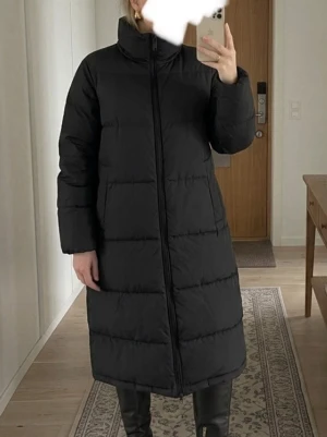 Svart lång dunjacka med hög krage - Säljer en svart lång dunjacka med hög krage och raka ärmar. Jackan har fyllning av 90% ankdun och 10% ankfjädrar, yttertyg i polyester och elastan. Stängs med dragkedja framtill och har en stilren, minimalistisk look.
