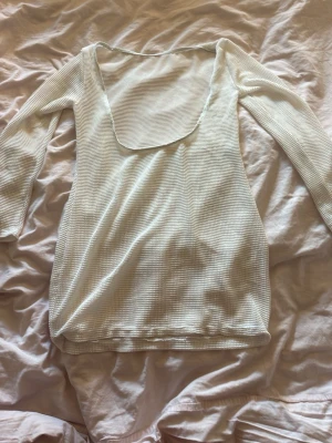 Vit coverup med öppen framsida - Säljer en vit coverup med ribbad struktur och lång ärm. Klänningen har en djup, öppen framsida som man kan ha bak även och är figurnära i modellen. Perfekt för dig som gillar minimalistisk och stilren design.