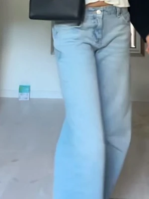 Ljusblåa vida jeans med låg midja - Säljer ett par ljusblå jeans med låg midja och breda, raka ben. Jeansen har klassisk femficksdesign och stängs med knapp och dragkedja. Perfekta för en avslappnad och trendig look.