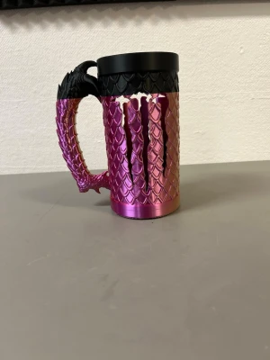Monster hållare  - Unik mugg med draktema i metall och plast. Muggen har fjällmönster i rosa, guld och svart samt ett handtag format som en draksvans. Perfekt för dig som gillar fantasy och vill ha något annorlunda till drycken.