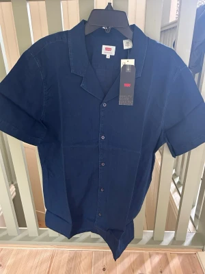 Mörkblå kortärmad skjorta Levi's - Säljer en mörkblå kortärmad skjorta från Levi's i klassisk modell. Skjortan har knappar framtill och en avslappnad krage. Tillverkad i mjuk bomull som känns skön mot huden. Perfekt för dig som gillar enkel och stilren design.