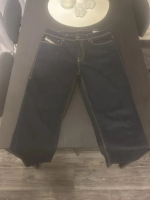Mörkblå diesel jeans - Säljer ett par mörkblå diesel jeans med raka ben och tydliga kontrastsömmar. Klassisk femficksmodell med normal midja och gylf med knapp. Jeansen har en enkel, stilren look och passar perfekt till en avslappnad vardagsstil.