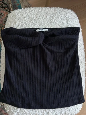 Svart ribbad tubtopp från NA-KD - Säljer en helt oanvänd svart ribbad tubtopp från NA-KD med en twistad detalj framtill🌸 har även en klister rand på insidan för att den ska sitta snyggt (se bild 2)🥰