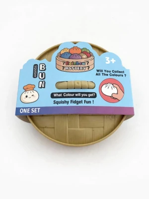 Squishy Bun Fidgetleksak - En squishy fidgetleksak formad som en ångad bulle i en rund bambukorg. Förpackningen har färgglad design och texten 'Rainbow Mystery'. Perfekt för dig som gillar att samla olika färger och vill ha något att klämma på när du är rastlös.