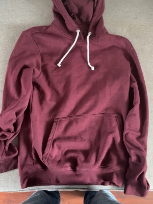 Vinröd hoodie från Pier One - Snygg vinröd hoodie från Pier One med klassisk känguruficka och vita dragsnören i huvan. Tillverkad i mjukt bomullsmaterial som känns skönt mot huden. Perfekt för chill dagar eller när du vill ha en avslappnad stil.
