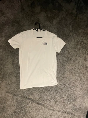 Vit t-shirt  - Säljer en klassisk vit t-shirt med liten logga på bröstet. T-shirten har rund halsringning och korta ärmar. Perfekt basplagg till garderoben och enkel att matcha med allt.