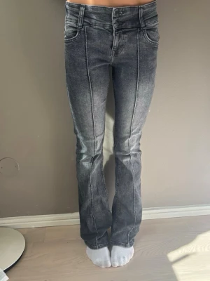 Grå bootcut jeans - Säljer ett par grå bootcut jeans med markerade pressveck framtill. Jeansen har hög midja, klassiska fem fickor och en lätt tvättad look. Perfekta för dig som vill ha en trendig och bekväm stil till vardags.