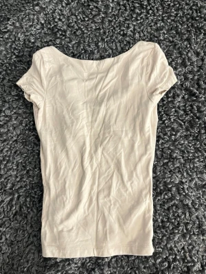 Beige topp med öppen rygg - Säljer en enkel och stilren beige topp i mjukt bomullsmaterial. Toppen har korta ärmar och en snygg öppen rygg som ger en trendig touch. Perfekt att matcha med jeans eller kjol för en clean look.