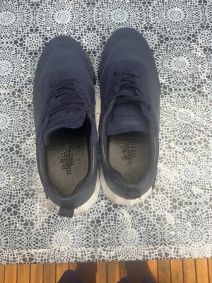 Marinblå sneakers med vit sula - Snygga marinblå sneakers med grov vit sula och matchande marinblå skosnören. Skorna har en modern design med rund tå och detaljer i både textil och syntetmaterial. Perfekta för dig som vill ha en stilren och sportig look.