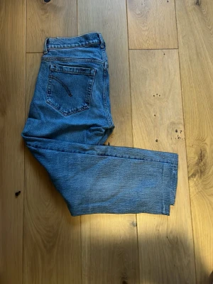 Blå raka jeans i klassisk modell - Säljer ett par blå jeans med rak passform och fem fickor. Jeansen har en klassisk look med normal midja och dragkedja. Materialet är denim i 100% bomull och färgen är en tvättad blå nyans som passar till det mesta.