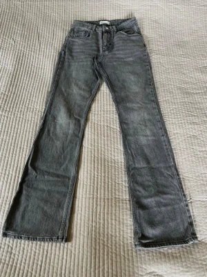 Grå bootcut jeans från Gina - Säljer ett par grå jeans med bootcut passform och relativ hög midja. Jeansen har dragkedja med knapp framtill. Materialet är denim i bomull och de har en snygg tvättad look. Perfekta för dig som gillar en avslappnad men trendig stil.