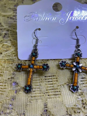 Korsörhängen med pärldetaljer - Säljer ett par unika örhängen i form av kors med orange och turkosa pärlor. Örhängena har silverfärgade detaljer och små blommor vid varje korsände. Perfekta för dig som vill sticka ut med accessoarerna!