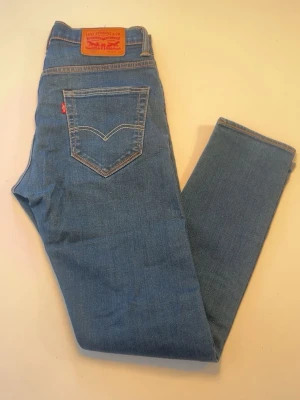 Blå Levi's jeans med rak passform - Klassiska blå jeans från Levi's med rak passform och fem fickor. Jeansen har den ikoniska läderlappen bak i midjan och kontrastsömmar. Tillverkade i slitstark denim med en snygg tvätt och normal midja. Perfekta för en avslappnad och tidlös stil. Levi Strauss & Co