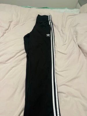 Svarta Adidas mjukisbyxor med ränder - Säljer ett par klassiska svarta Adidas mjukisbyxor. Dessa har jag bara använt 3-4 gånger.  