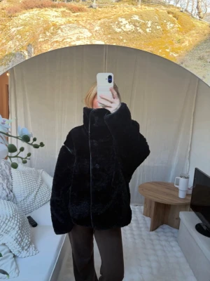Svart oversized jacka - Säljer en svart teddyjacka med hög krage och oversized passform. Jackan har stora ärmar och stängs med knappar framtill. Materialet är fluffigt och mjukt.