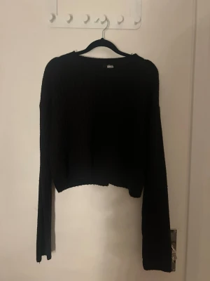 Svart croppad stickad tröja M - Säljer en svart croppad stickad tröja med långa ärmar och rund hals. Tröjan har ribbstickade muddar och en enkel, stilren design som passar perfekt till jeans eller kjol. Materialet känns mjukt och bekvämt mot huden.
