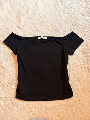 Svart off shoulder topp - En svart off shoulder topp med korta ärmar och figurnära passform. Toppen har en bred urringning som sitter snyggt över axlarna och är gjord i ett mjukt, stretchigt material. Perfekt att styla med jeans eller kjol för en trendig look. Aldrig använd, nyskick utan prislapp.                        Kontakta för fler bilder/frågor💕