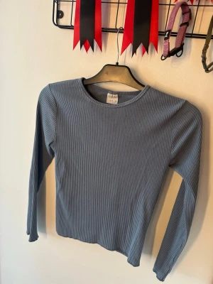 Ribbad blå långärmad topp Zara - Säljer en ribbad långärmad topp från Zara i en snygg blå färg. Tröjan har rund halsringning och är tillverkad i ett stretchigt, mjukt material som sitter skönt på kroppen. Perfekt att styla med jeans eller kjol för en enkel men trendig look.