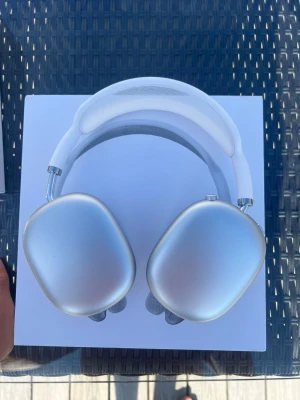 Vita AirPods Max - Snygga vita over-ear hörlurar med mjuka, grå mesh-kuddar och justerbart huvudband. Hörlurarna har en modern, minimalistisk design med aluminiumkåpor och detaljer i metall. Perfekta för dig som vill ha både stil och bra ljud i vardagen. Jag är osäker på äktheten därav att jag inte har nått kvitto! 