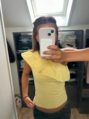 Gul topp med volang och one shoulder - Snygg gul topp med en axel och stor volangdetalj som går diagonalt över bröstet. Toppens material är mjukt och stretchigt. Från Kappahl i storlek 170 och inte använd många gånger. Kom privat om du vill se fler bilder i andra vinklar och pris kan diskuteras💗