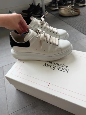 Vita Alexander McQueen sneakers - Stilrena vita sneakers från Alexander McQueen med svart detalj på hälen och tjock sula. Skorna har klassisk snörning och perforerade hål på sidorna för ventilation. Perfekta för dig som vill ha en clean och trendig look.