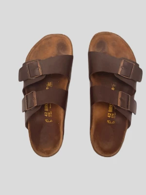 Bruna Birkenstock sandaler i läder - Klassiska bruna sandaler från Birkenstock med två breda remmar i läder och justerbara metallspännen. Fotbädden är formad för extra komfort och sulan har ett vågigt mönster för bra grepp. Perfekta för en avslappnad och stilren look.