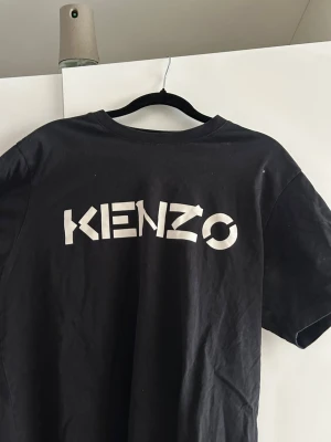 Svart Kenzo t-shirt med logga - Säljer en svart t-shirt från Kenzo med stor vit logga tryckt på bröstet. Klassisk rund halsringning och korta ärmar. Perfekt till jeans eller shorts för en clean och trendig look.