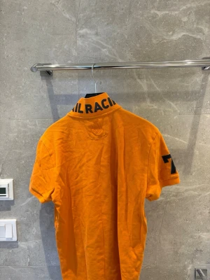 Orange kortärmad t-shirt,sail racing - Snygg orange t-shirt med korta ärmar och tryckta detaljer på kragen och ärmen. T-shirten har knappar vid halsen och en liten logga på bröstet. Perfekt för dig som vill sticka ut med färg och stil.