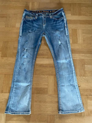 Vintage Rock Revival jeans - Sjukt snygga boot cut jeans från Rock Revival i storlek 33. Är i grymt bra skick med perfekta fades och slitningar på låren och alla knappar sitter kvar. Ny pris var ca 2700kr. Priset är inte hugget i sten. Hör gärna av dig om du har några funderingar. 