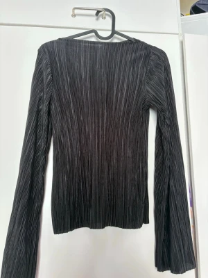 Svart ribbad långärmad topp - Säljer en svart långärmad topp med ribbad struktur. Toppen har en smal passform och är tillverkad i ett stretchigt material som sitter snyggt på kroppen. Perfekt att styla med jeans eller kjol för en trendig look. Utsvängda ärmar🙏🏻