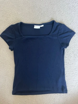 Mörkblå topp med fyrkantig ringning - En enkel och stilren mörkblå topp med korta ärmar och fyrkantig ringning. Tillverkad i mjukt bomullsmaterial och har en normal passform. Perfekt att matcha med jeans eller kjol för en clean look.