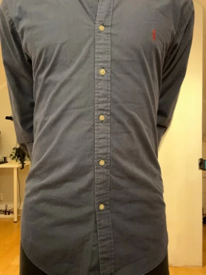 Blå Ralph lauren skjorta  - Ralph lauren skjorta i storlek L slimfit. Modellen är 175 väger 65kg och har storlek S. Den har en lagning på ärmen. Längd 70cm bredd 48cm armlängd 62cm 
