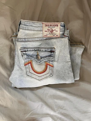True Religion - Säljer ett par ljusblå bootcut jeans från True Religion med ikoniska kontrastsömmar och broderad ficka bak. Jeansen har låg midja, och passar perfekt nu till hösten❣️jeansen har inget slitage och ser nästan nya ut. 