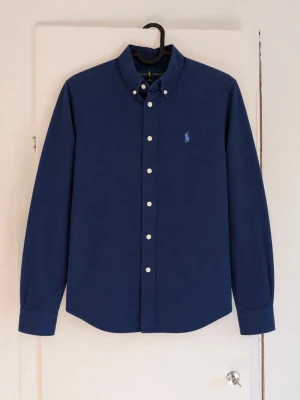 Ralph Lauren skjorta - Säljer en mörkblå skjorta från Ralph Lauren i fint skick. Klassisk button-down-modell med broderad logga på bröstet. Perfekt både till vardags och för mer uppklädda tillfällen. • Färg: mörkblå • Märke: Ralph Lauren • Modell: button-down • Skick: mycket fint, utan synliga defekter • Passar perfekt till både jeans och chinos