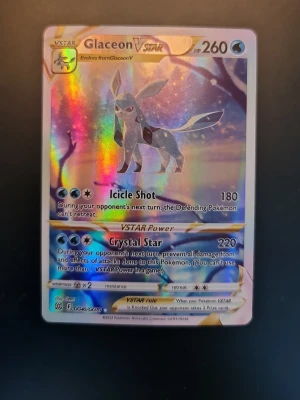 Glaceon VSTAR Pokémonkort holo - Säljer ett Glaceon VSTAR Pokémonkort med holografisk yta. Kortet har en färgstark design med blå, lila och silvertoner och visar Glaceon i en isig miljö. Kortet är tillverkat av laminerad kartong och har unika attacker och VSTAR Power.