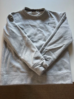 Grå sweatshirt från Sail Racing - En stilren grå sweatshirt från Sail Racing med rund halsringning och diskret logga på bröstet. Tröjan har långa ärmar och mjukt material som känns skönt mot huden. Perfekt för en avslappnad look.