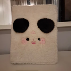 Kpop binder a4 - Unik anteckningsbok med mjukt, vitt fluffigt omslag och ett gulligt pandamotiv på framsidan. Boken har stora svarta ögon, rosa kinder och små broderade detaljer. På baksidan står det 'hisocute' i ett rosa moln. Perfekt för anteckningar eller dagbok. Kan även användas som en binder. 