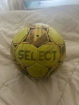 Gul SELECT fotboll AG - Säljer en gul SELECT fotboll, modell Flash Turf, som är anpassad för spel på konstgräs (AG). Bollen har tryckta detaljer i svart och orange samt FIFA Quality-märkning. Perfekt för dig som vill ha en boll för träning eller match på konstgräs.