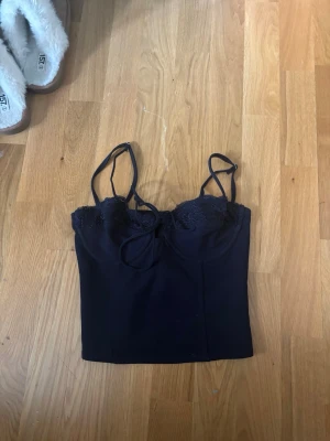 Svart linnetopp från Edikted - Snygg svart linnetopp från Edikted med tunna axelband och spetsdetaljer upptill. Toppen har en croppad passform och är perfekt för att styla med höga jeans eller kjol. Materialet känns mjukt och följsamt.