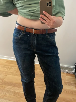 Mörkblå raka jeans med bruna sömmar - Säljer ett par mörkblå jeans med raka ben och klassiska fem fickor. Jeansen har kontrasterande bruna sömmar och normal midja. Materialet är kraftigt denim som ger en tidlös look. Perfekta till vardagsstilen och funkar året runt.