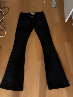 Svarta bootcut jeans  - Snygga svarta bootcut jeans med vita kontrastsömmar på bakfickorna. Jeansen har låg midja och utsvängda ben, vilket ger en retro och trendig look. Tillverkade i ett stretchigt denimtyg för extra komfort.