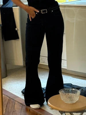 mörkblåa bootcut jeans med hög midja - Säljer ett par mörkblåa bootcut jeans med hög midja och utsvängda ben. Jeansen har klassiska fickor fram och bak samt kontrastsömmar. Materialet är denim med lite stretch för skön passform. Perfekta till en trendig och avslappnad look.
