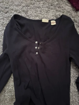 Svart långärmad henley topp - En svart långärmad henley topp med rundad halsringning och fyra små knappar framtill. 