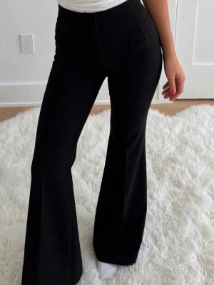 Svarta wide kostymbyxor - Säljer ett par svarta kostymbyxor med hög midja och vida/raka ben. Byxorna har en stilren look med diskreta sömmar framtill och passpoalfickor bak. Perfekta för dig som gillar en trendig och clean stil.