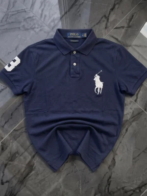 Navy Blue Polo Ralph Lauren Mens Size M - Mens M - Very Good Condition - A classic Navy Blue Polo from Ralph Lauren in a men’s medium. It’s in very good shape with no holes, stains, or defects—just a clean, timeless piece that works well for casual or smart casual looks. Perfect if you’re after something versatile and reliable.  Authentic item. Fast shipping. Message with questions. 