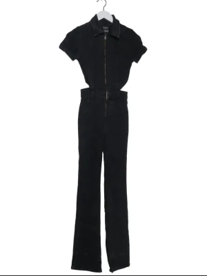 Svart jumpsuit med dragkedja - Snygg svart jumpsuit i denim-look med korta ärmar, krage och dragkedja framtill. Modellen har raka ben och bälteshällor i midjan. 