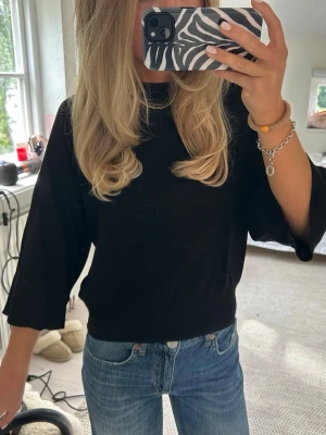 Svart topp med vida ärmar - En svart topp med rund hals och vida trekvartsärmar. Modellen är loose fit och toppen har en enkel, stilren design som passar till mycket. Perfekt att matcha med jeans eller kjol för en avslappnad look. Aldrig använd med prislapp kvar!
