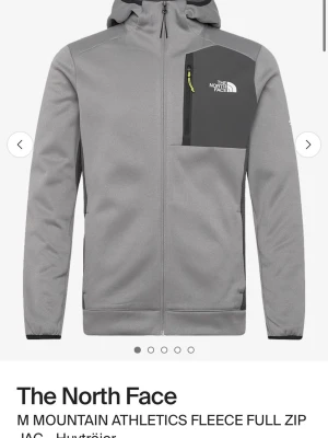 Grå fleecejacka från The North Face - Snygg grå fleecejacka från The North Face med hel dragkedja och huva. Jackan har en mörkare grå bröstficka med logga och gul detalj på dragkedjan. Perfekt för lager-på-lager och outdoor-aktiviteter.