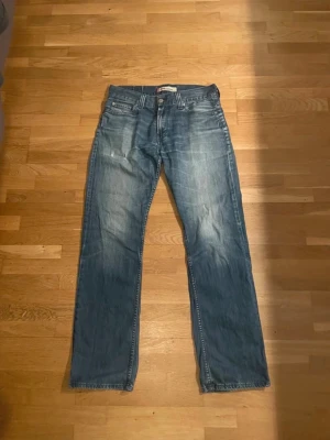 Levis 506 Standard Straight Fit Jeans 2000/USA-stil Vintage 90 tals tvättade Denim - Säljer ett par klassiska blå jeans från Levi's med rak passform och fem fickor. Jeansen har en ljus tvätt med slitningar och tydliga sömmar. Perfekta för en avslappnad och tidlös stil.